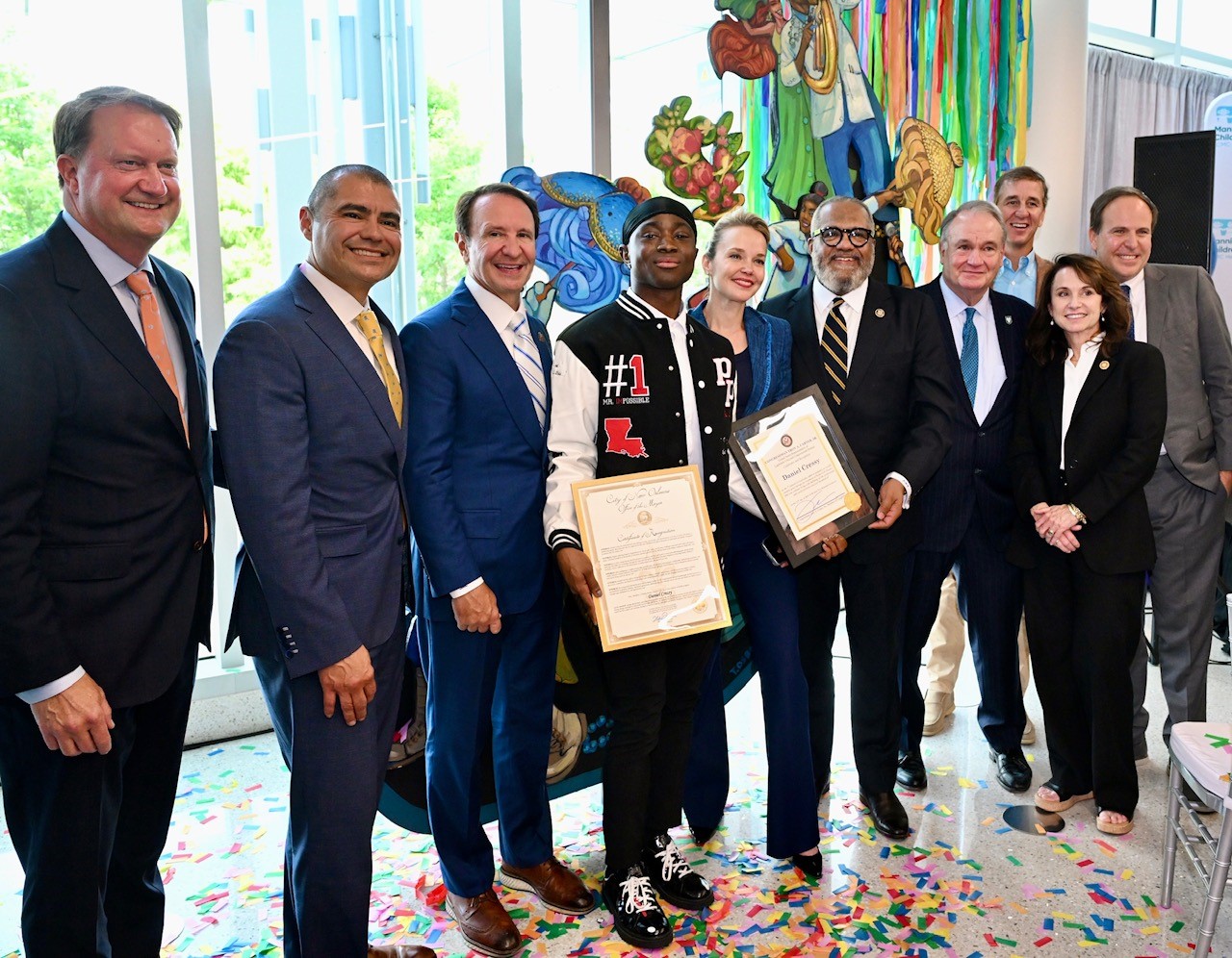 A young man and woman receive awards from officials in a festive, confetti-covered room.