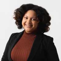 Smiling woman with dark curly hair and braces, wearing black blazer over rust top.